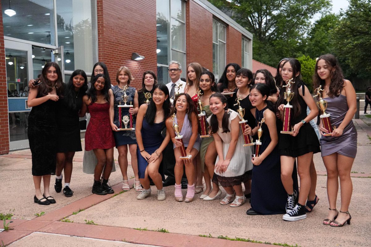 Girls varsity track team and Coach Timothy Connor posing for the camera with trophies outside during sports awards.