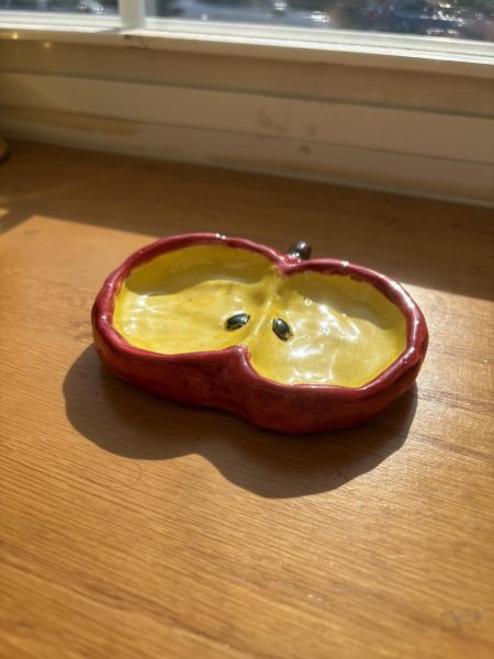 A ceramic dish shaped and painted to resemble a halved apple, showcasing student work from a recent pottery project completed in the Ceramics club.
